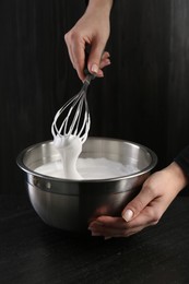 Woman making whipped cream with whisk at black table, closeup