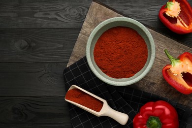 Photo of Bowl of aromatic paprika and fresh peppers on black wooden table, flat lay. Space for text