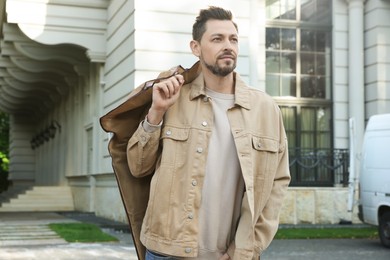 Photo of Attractive serious man holding garment cover with clothes outdoors. Dry cleaning service