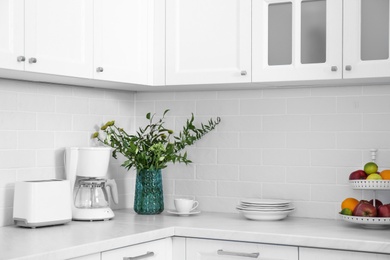 Modern toaster, coffeemaker and dishware on countertop in kitchen