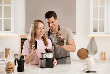 Photo of Lovely couple using electric coffee grinder together in kitchen