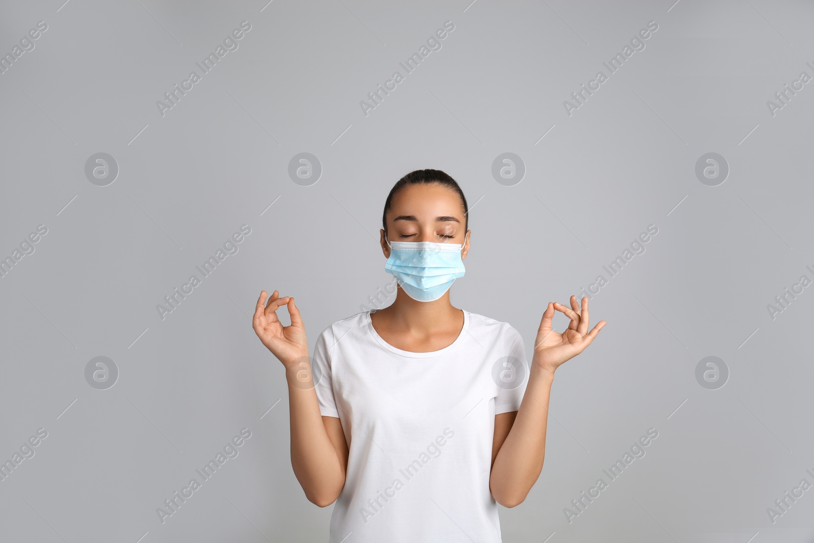Photo of Woman in protective mask meditating on grey background. Dealing with stress caused by COVID‑19 pandemic