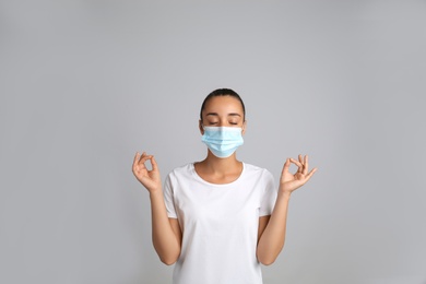 Photo of Woman in protective mask meditating on grey background. Dealing with stress caused by COVID‑19 pandemic