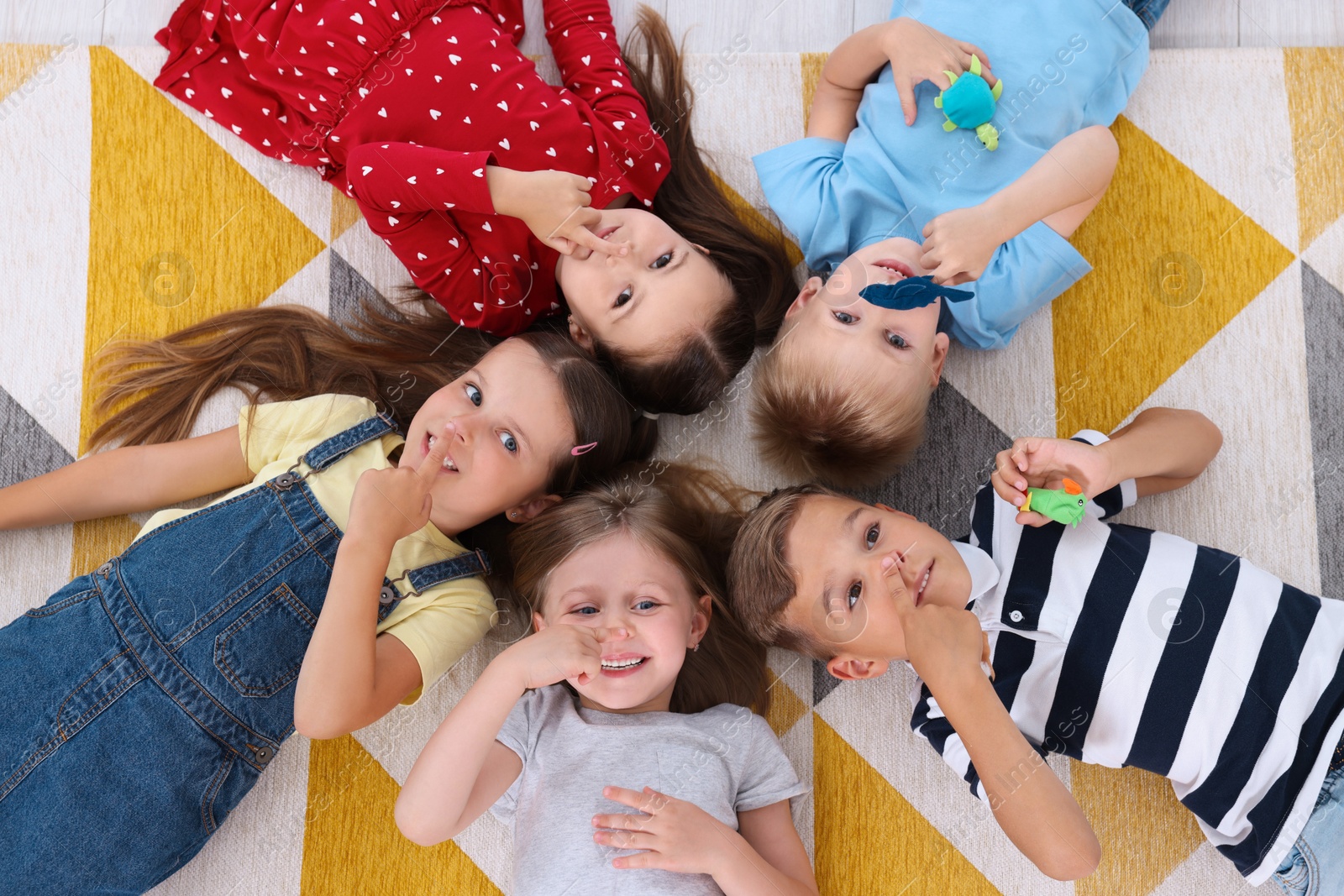 Photo of Adorable little children lying on bright carpet together in kindergarten, top view. Playtime activities