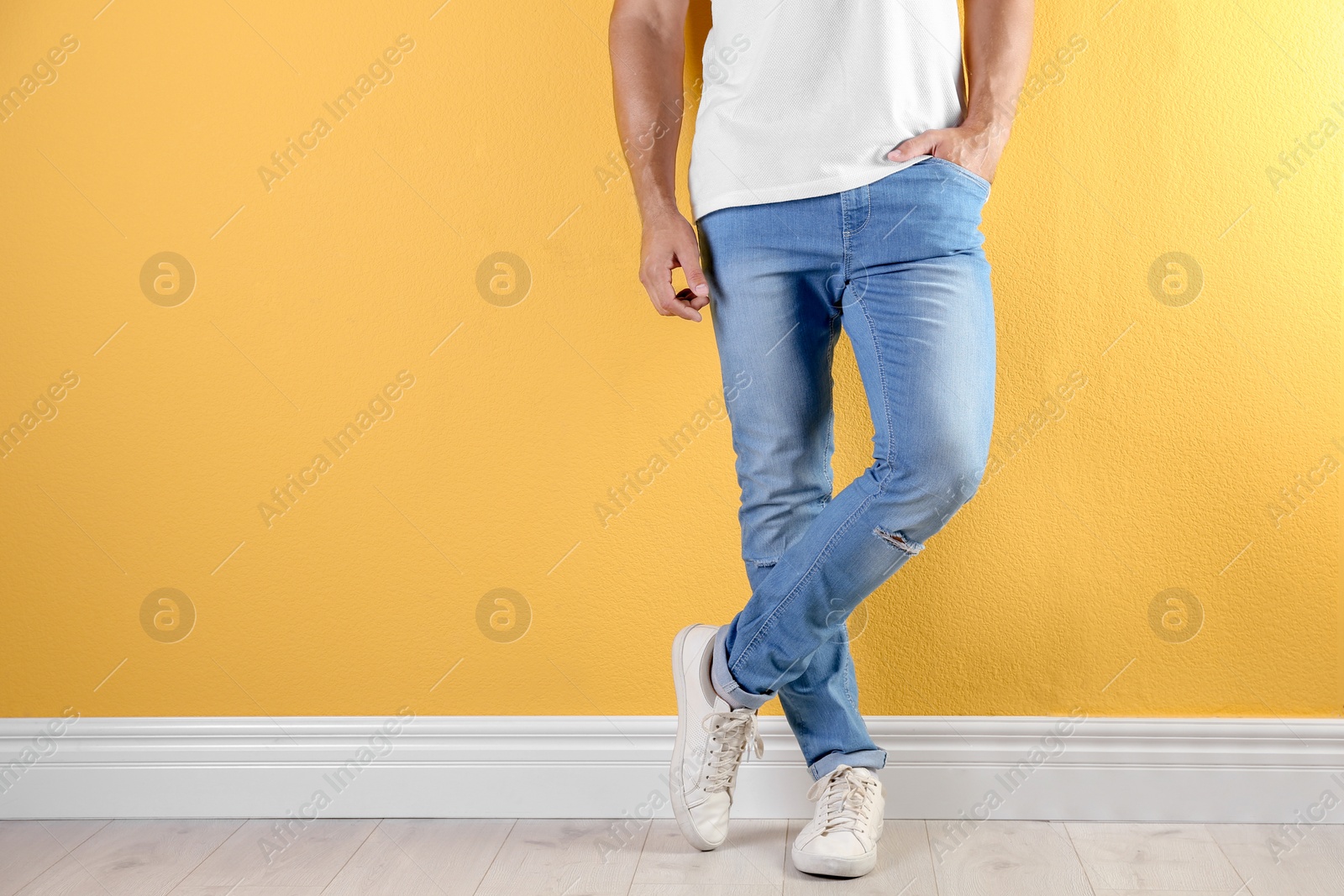 Photo of Young man in stylish jeans near color wall with space for text, focus on legs