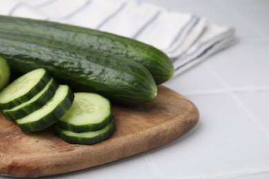 Fresh whole and cut cucumbers on white tiled table, closeup. Space for text