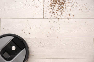 Photo of Modern robotic vacuum cleaner removing scattered buckwheat from wooden floor, top view. Space for text