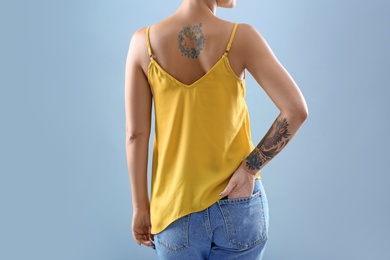 Young woman with tattoos on color background