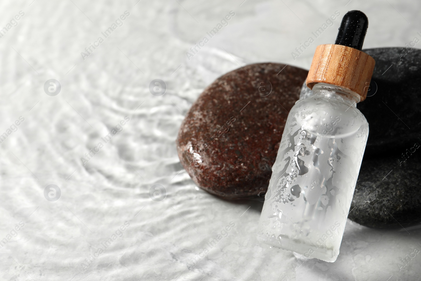 Photo of Bottle of face serum and spa stones in water on light background, closeup. Space for text