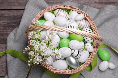 Photo of Easter eggs in basket and lilac flowers on wooden table, flat lay