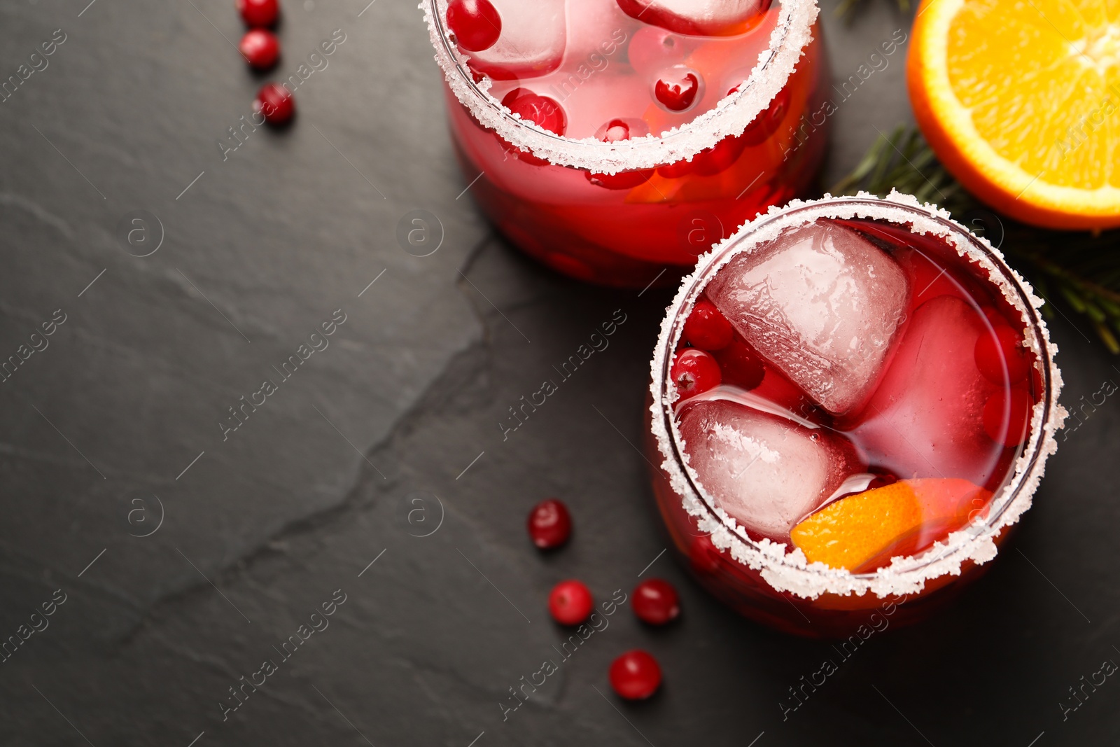 Photo of Tasty cranberry cocktail with ice cubes in glasses on dark gray textured table, flat lay. Space for text