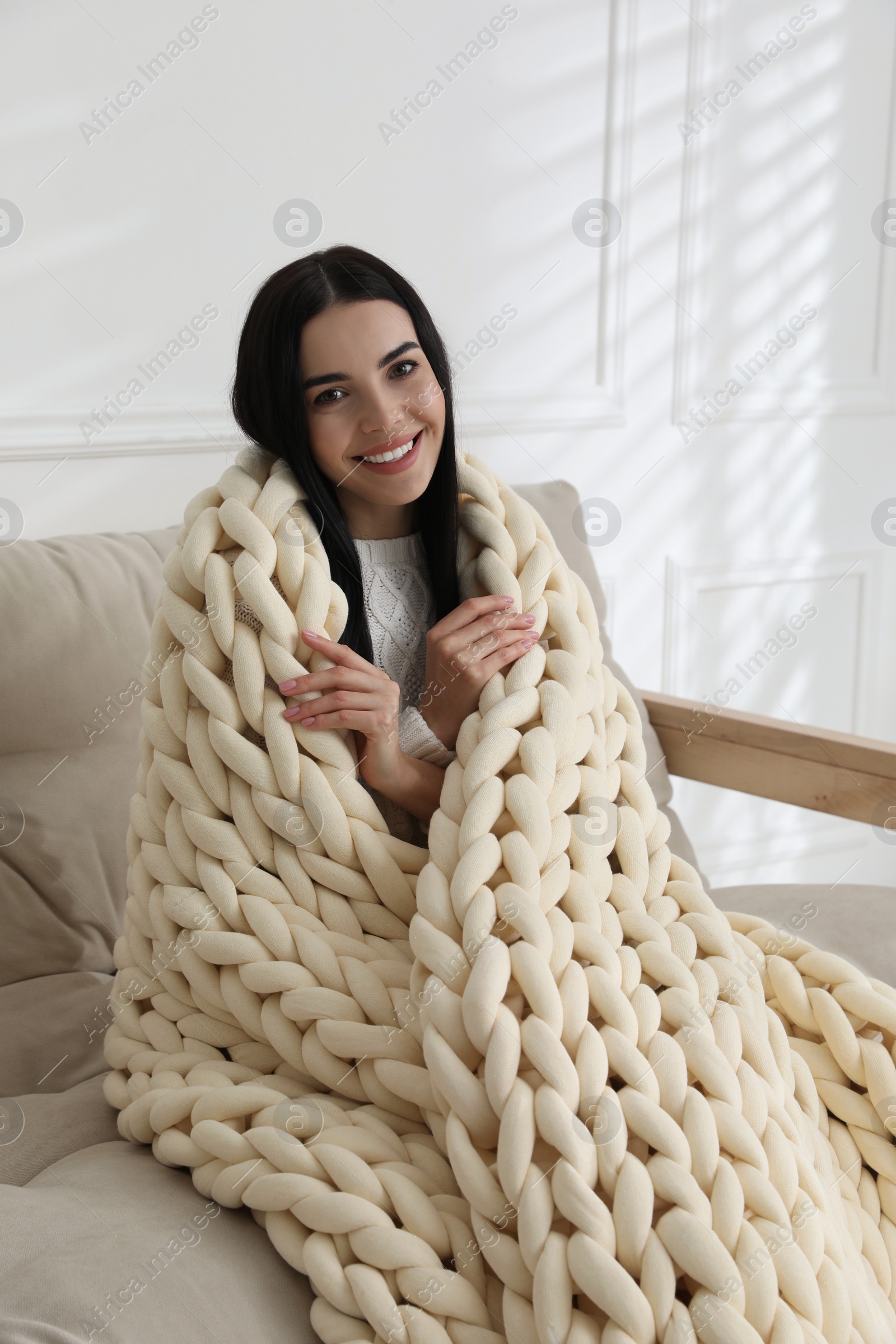 Photo of Young woman with chunky knit blanket on sofa at home