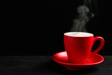 Image of Red cup with hot steaming coffee on dark table against black background, space for text