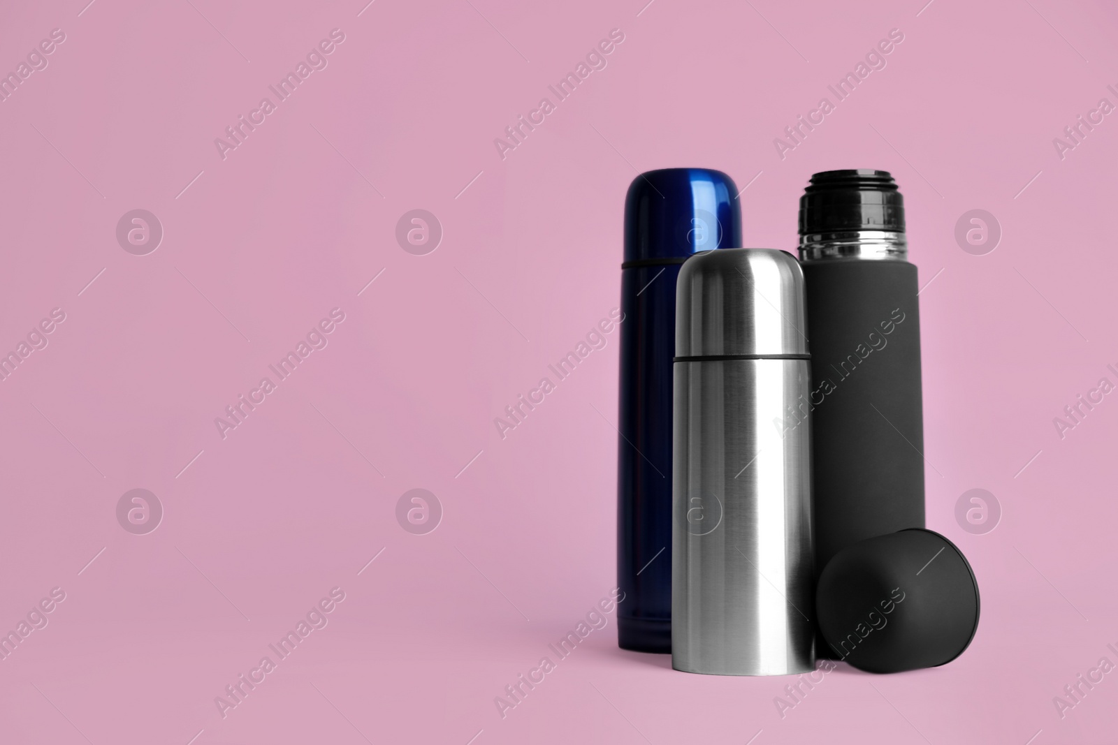 Photo of Stylish thermo bottles on pink background, space for text