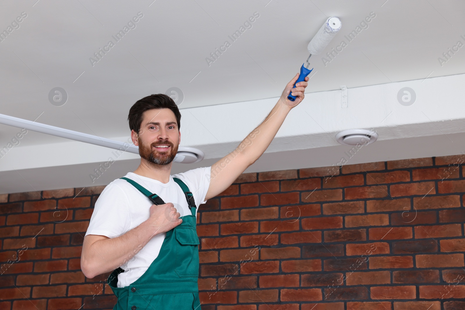 Photo of Handyman painting ceiling with roller in room