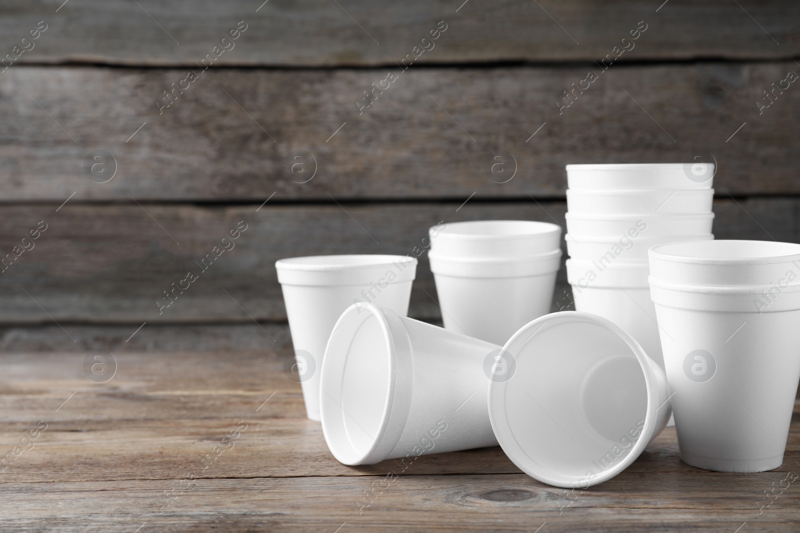 Photo of Many white styrofoam cups on wooden table, space for text