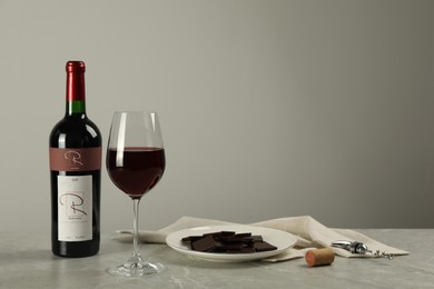 Photo of Bottle and glass of red wine with chocolate on light marble table. Space for text