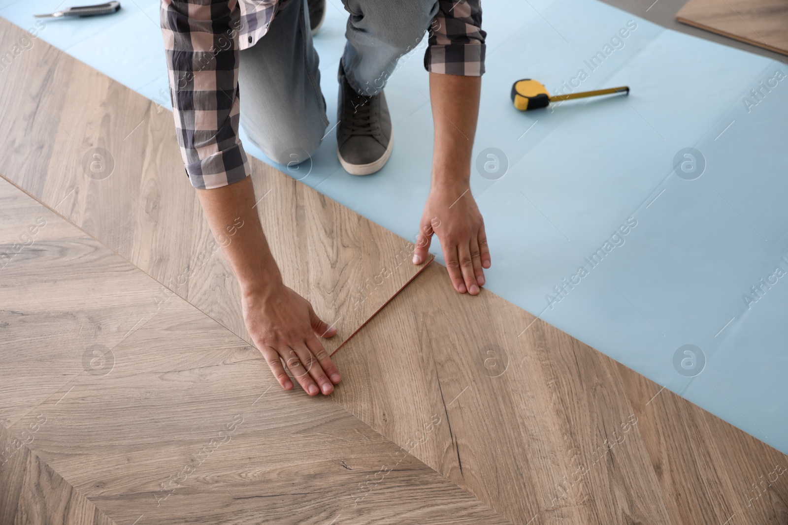 Photo of Worker installing laminated wooden floor indoors, closeup