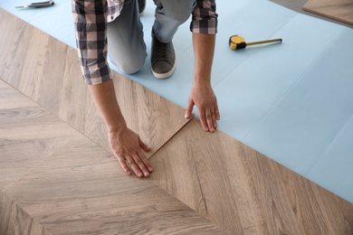 Worker installing laminated wooden floor indoors, closeup