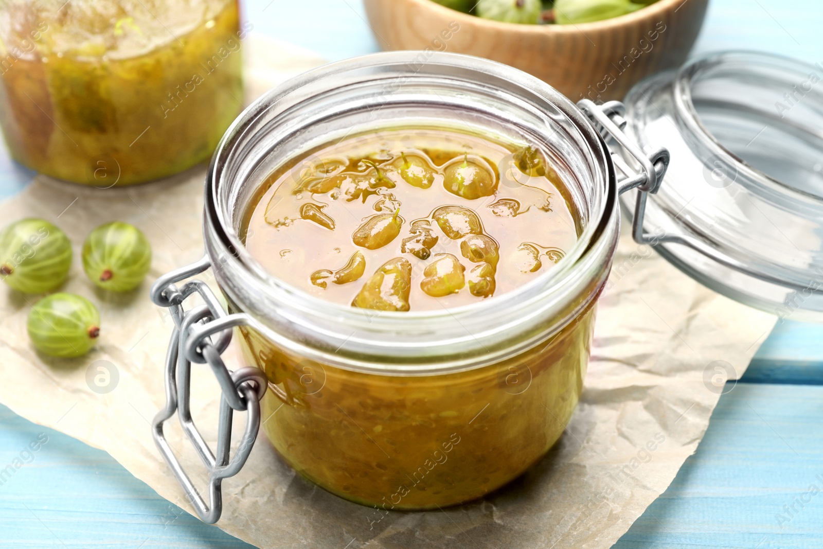 Photo of Jar of delicious gooseberry jam and fresh berries on blue wooden table, closeup