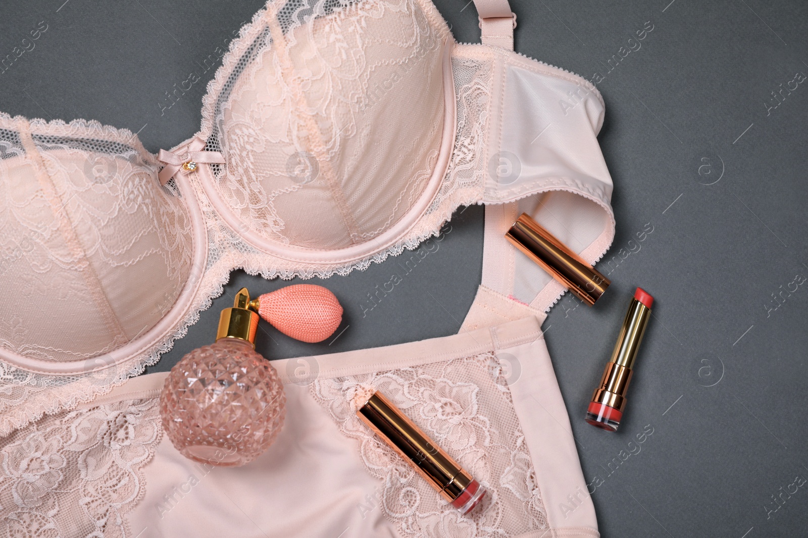 Photo of Elegant beige plus size women's underwear, lipsticks and perfume on grey background, flat lay