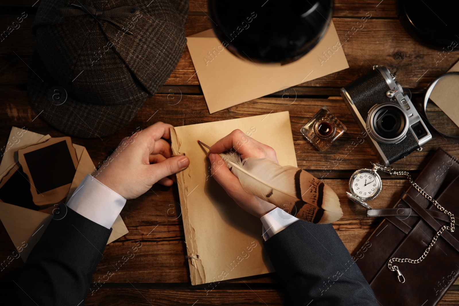 Photo of Detective writing with feather on paper at wooden table, top view