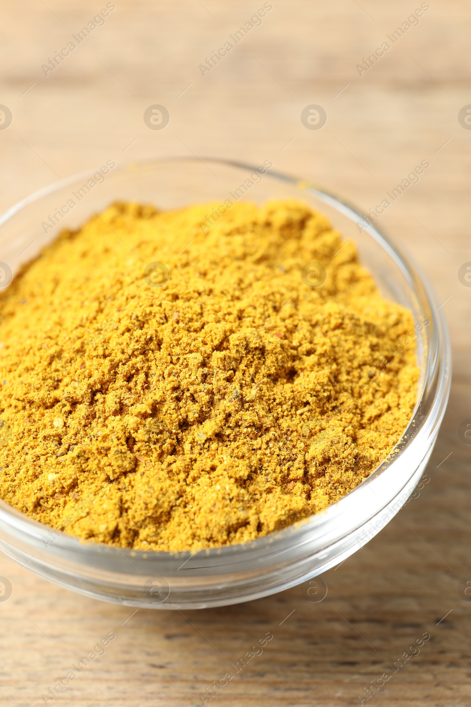 Photo of Curry powder in bowl on wooden table, closeup