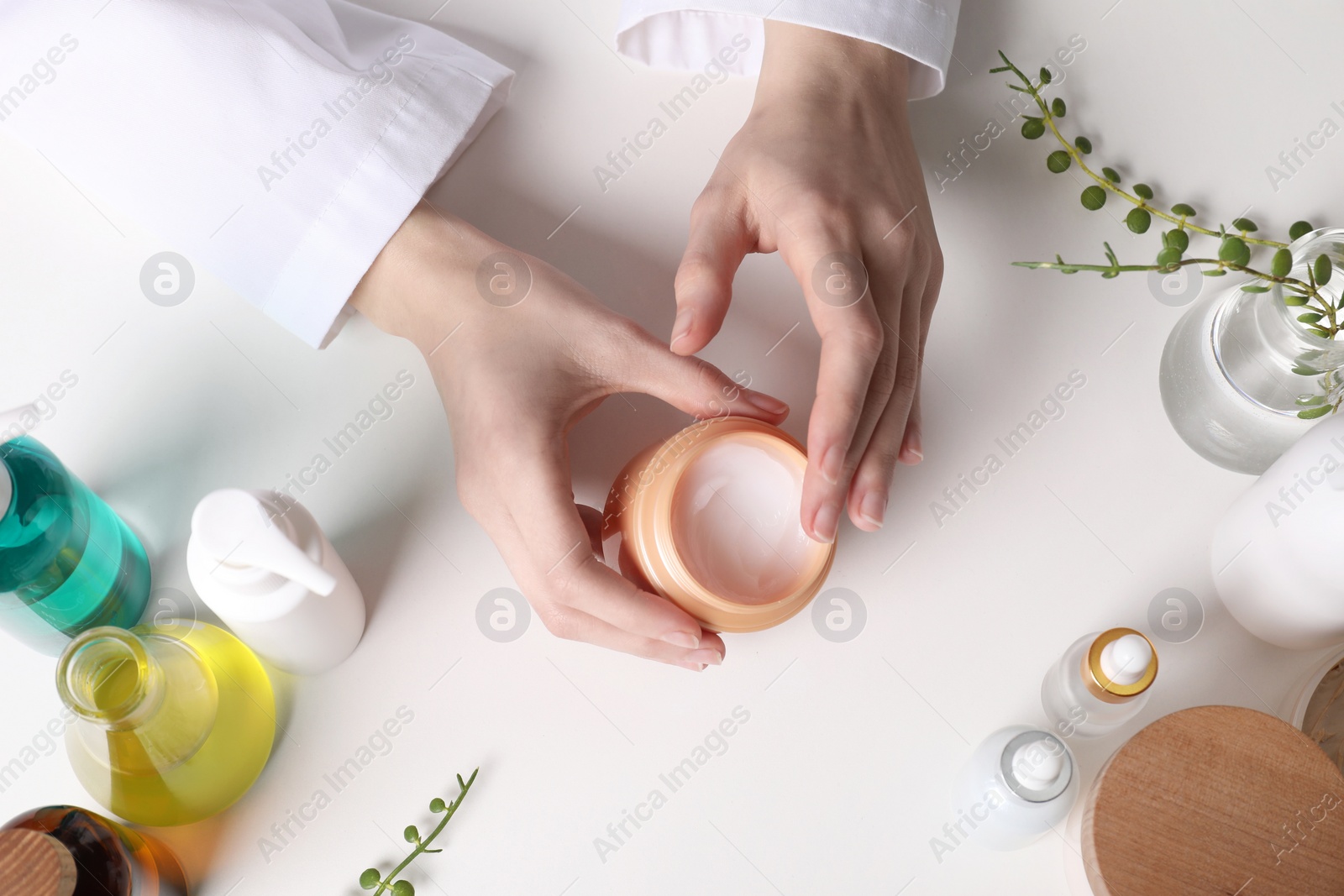 Photo of Dermatologist with jar testing cosmetic product at white table, top view