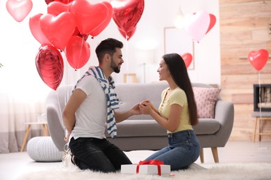 Photo of Happy young couple with heart shaped balloons in living room. Valentine's day celebration
