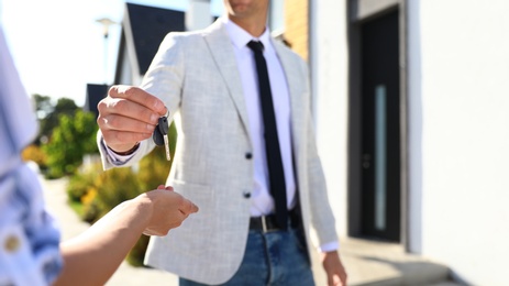 Real estate agent giving house keys to young woman outdoors, closeup