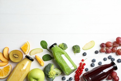 Bottles of delicious juices and fresh fruits on white wooden table, flat lay. Space for text