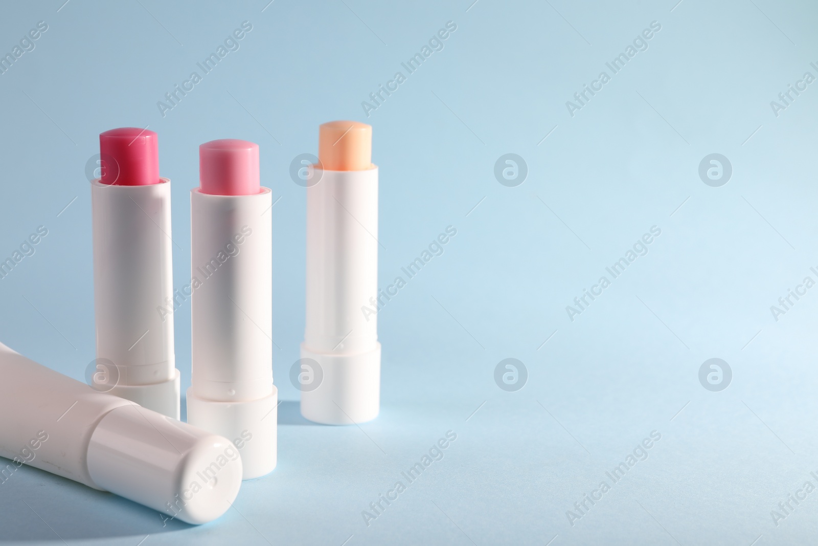Photo of Different lip balms on light blue background, space for text