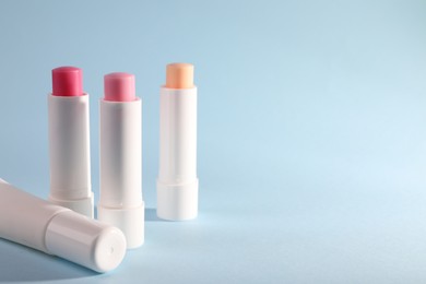 Different lip balms on light blue background, space for text