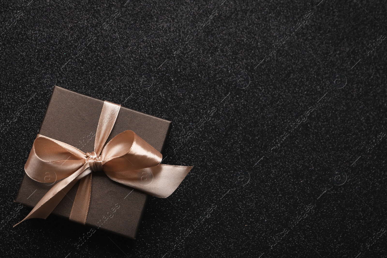 Photo of Gift box with golden bow on black background, top view. Space for text