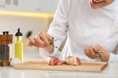 Photo of Professional chef decorating delicious meat with thyme at white marble table, closeup