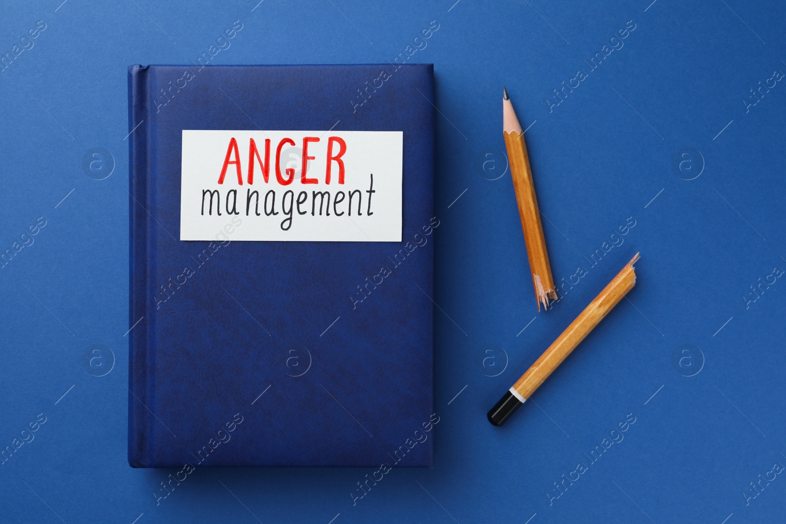 Photo of Notebook with words Anger Management and broken pencil on blue background, flat lay
