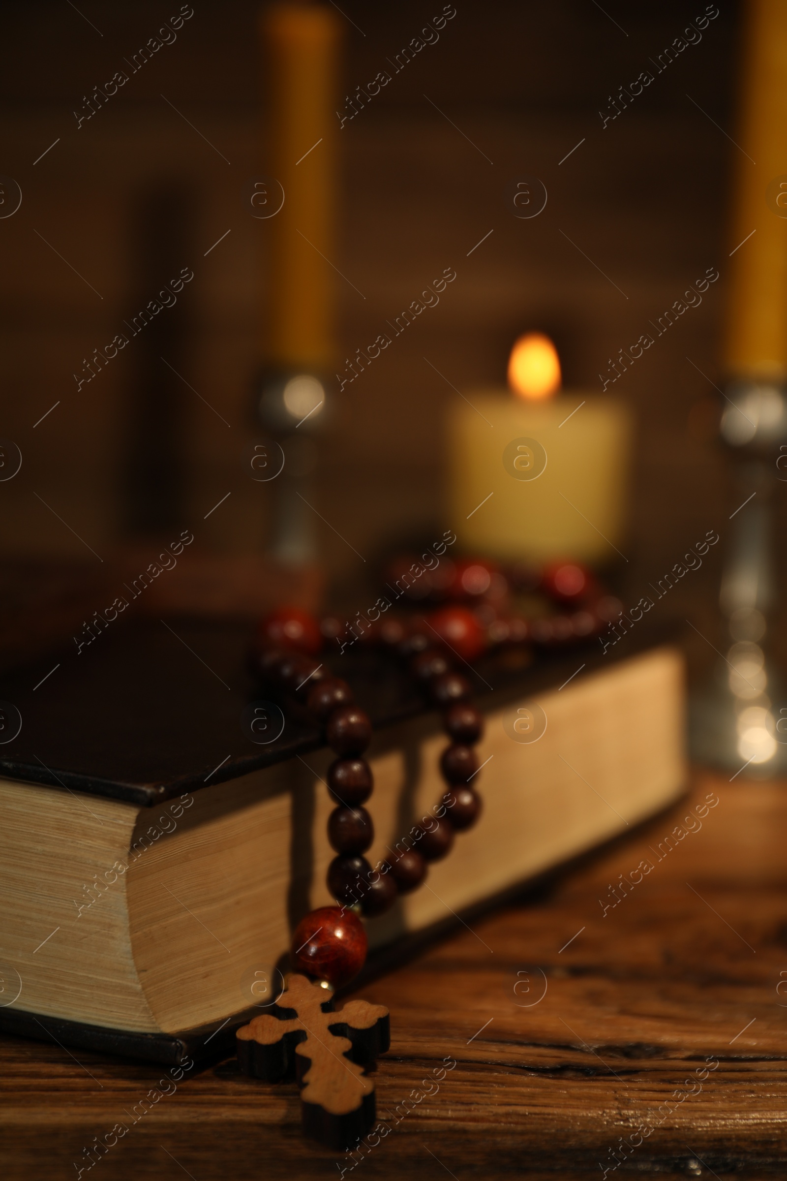 Photo of Cross, Bible, rosary beads and church candles on wooden table, closeup
