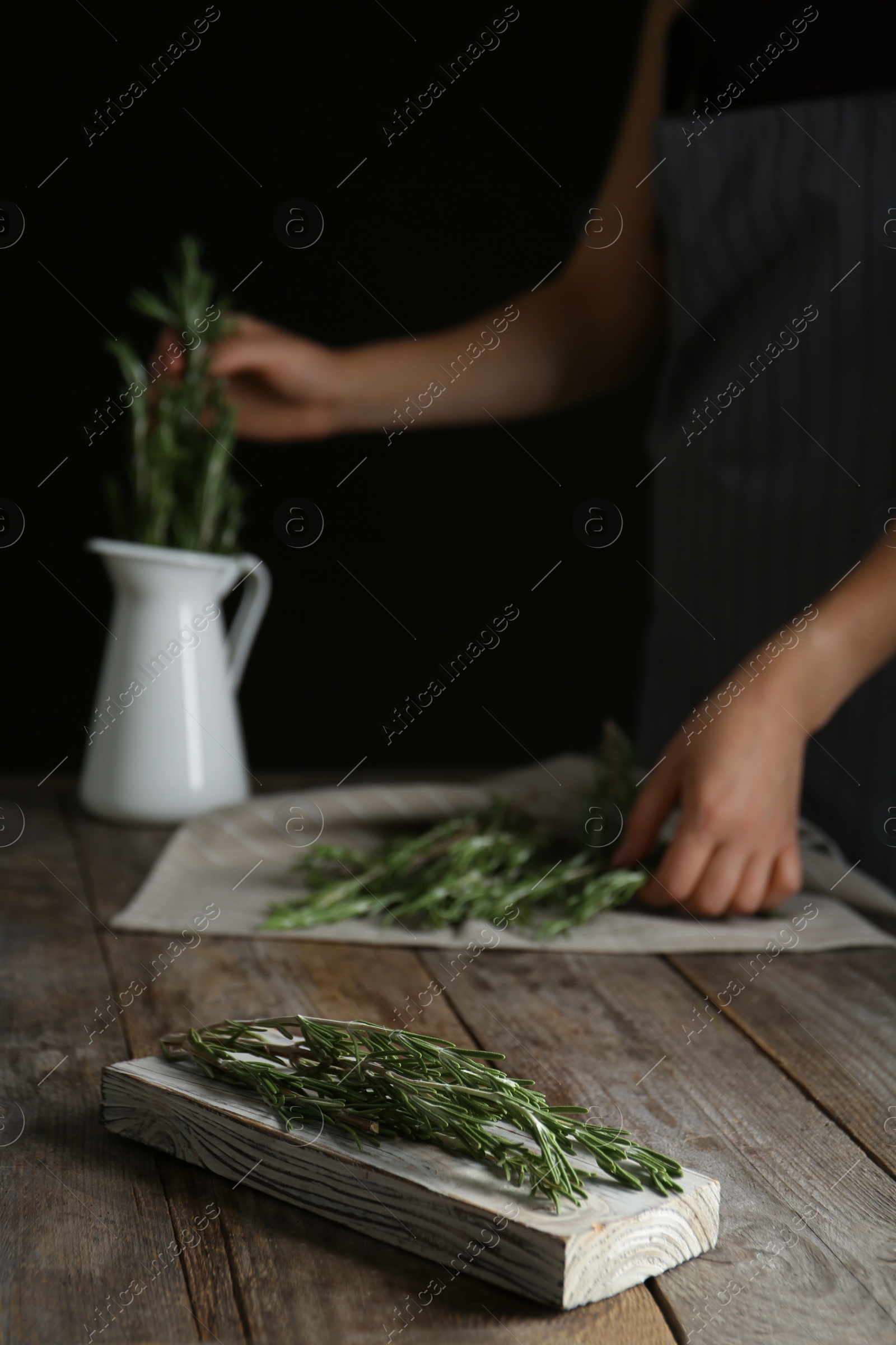 Photo of Wooden board with fresh green rosemary and woman on background. Aromatic herbs