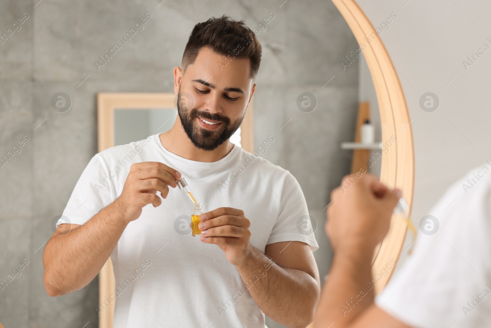 Photo of Handsome man with serum in his hands near mirror indoors