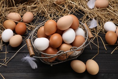 Fresh chicken eggs and dried straw on black wooden table