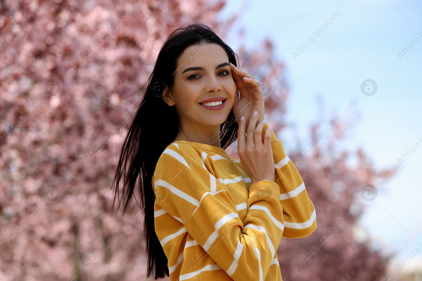 Photo of Pretty young woman near beautiful blossoming trees outdoors. Stylish spring look