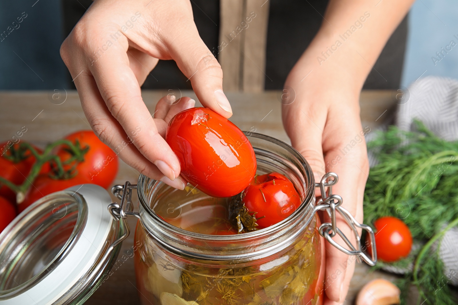 Photo of Woman taking pickled tomato from glass jar at table, closeup view