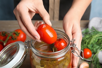 Woman taking pickled tomato from glass jar at table, closeup view
