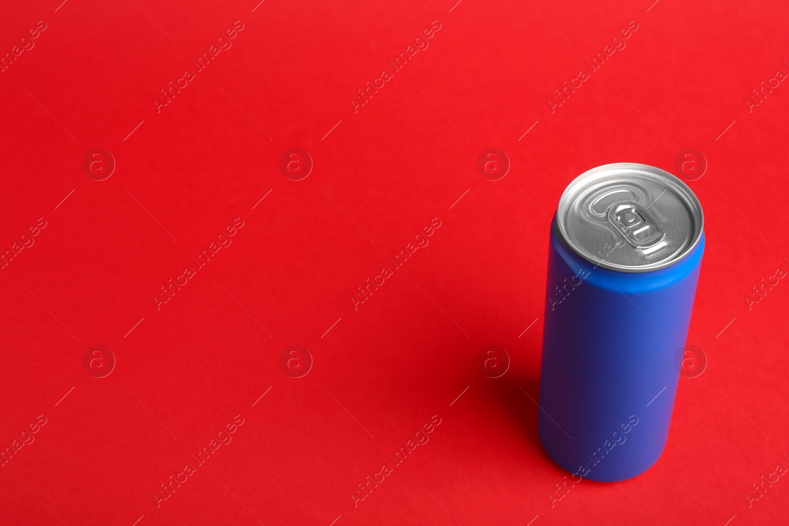 Photo of Energy drink in blue can on red background, space for text