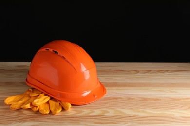 Hard hat and gloves on wooden table, space for text. Safety equipment
