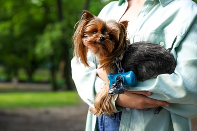 Photo of Woman holding her cute dog with waste bags in park, closeup. Space for text