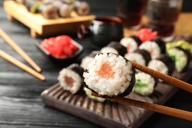 Photo of Set of delicious sushi rolls and chopsticks on black wooden table, closeup. Space for text