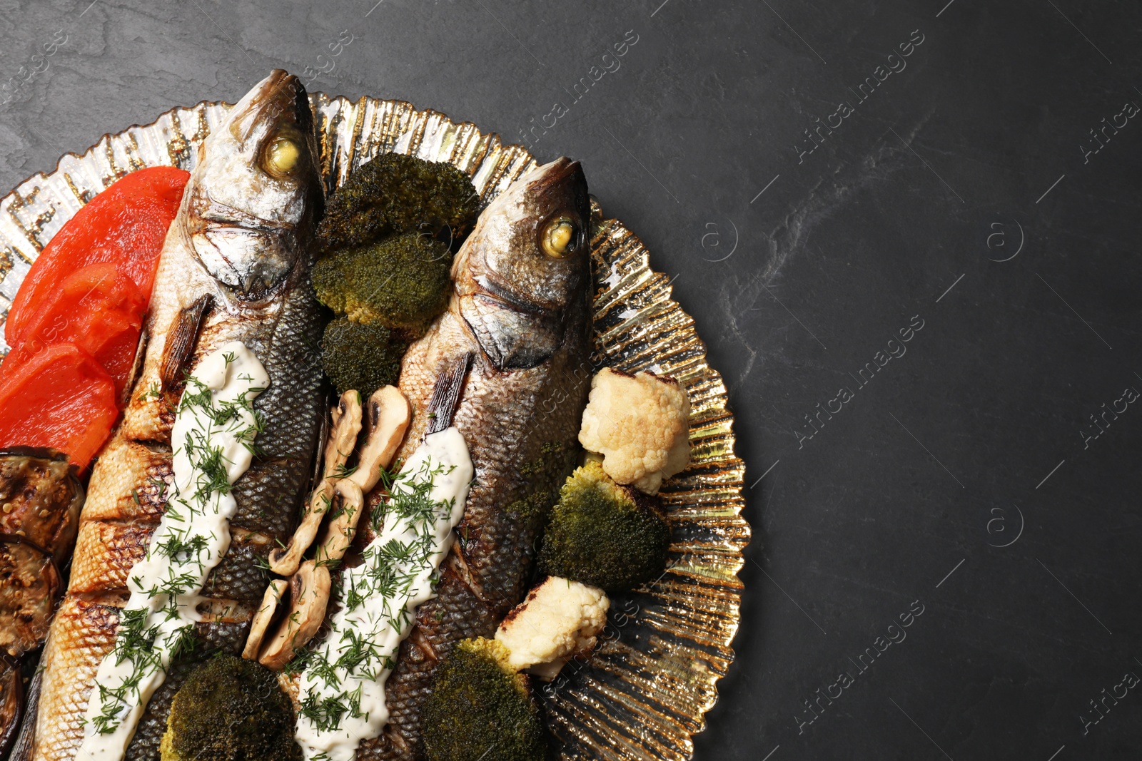 Photo of Plate with delicious sea bass fish and ingredients on dark grey table, top view. Space for text