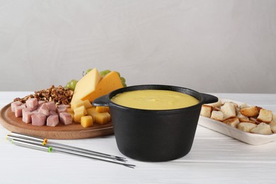 Fondue with tasty melted cheese, forks and different products on white wooden table