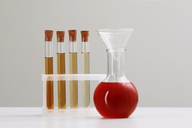 Photo of Different laboratory glassware with brown liquids on white table against light background